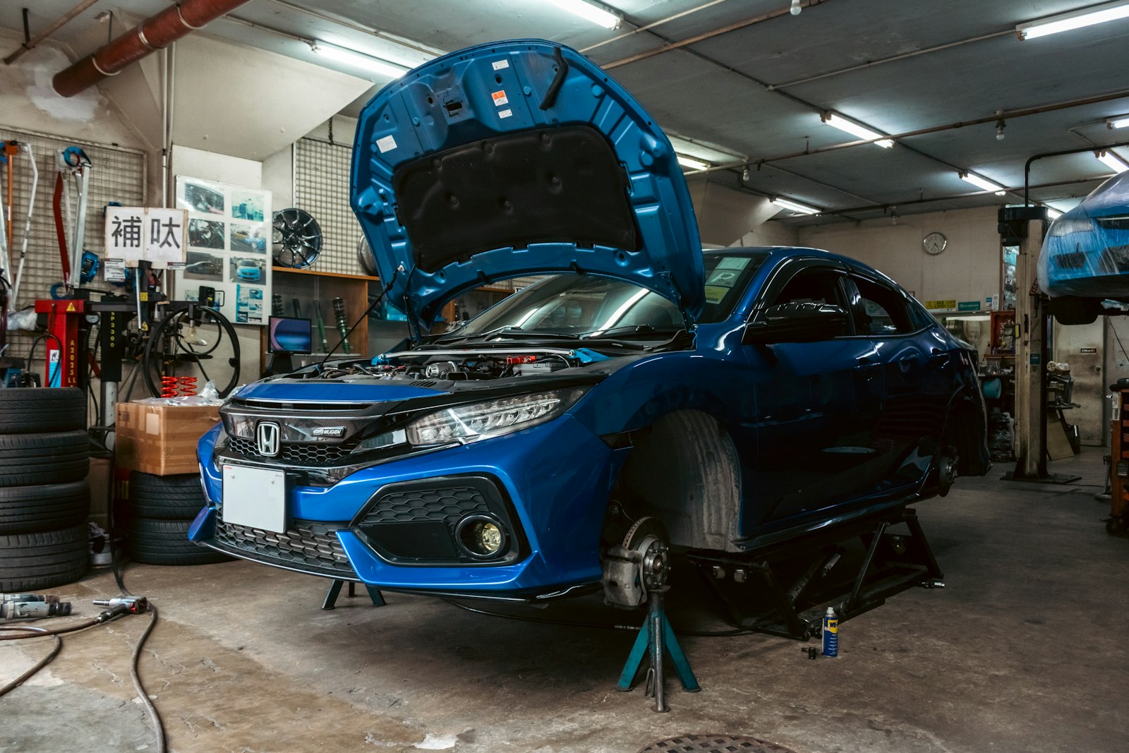 Blue car with its hood open on stands in a repair shop