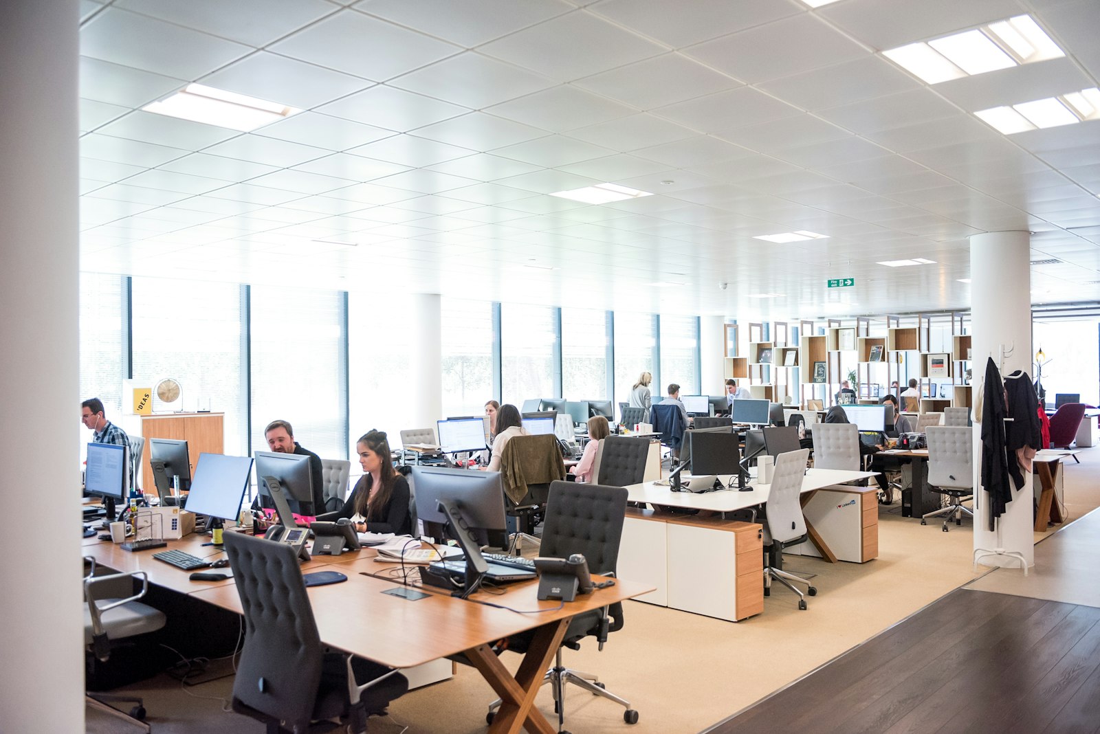 People working at desks with monitors and phones in a bright open office